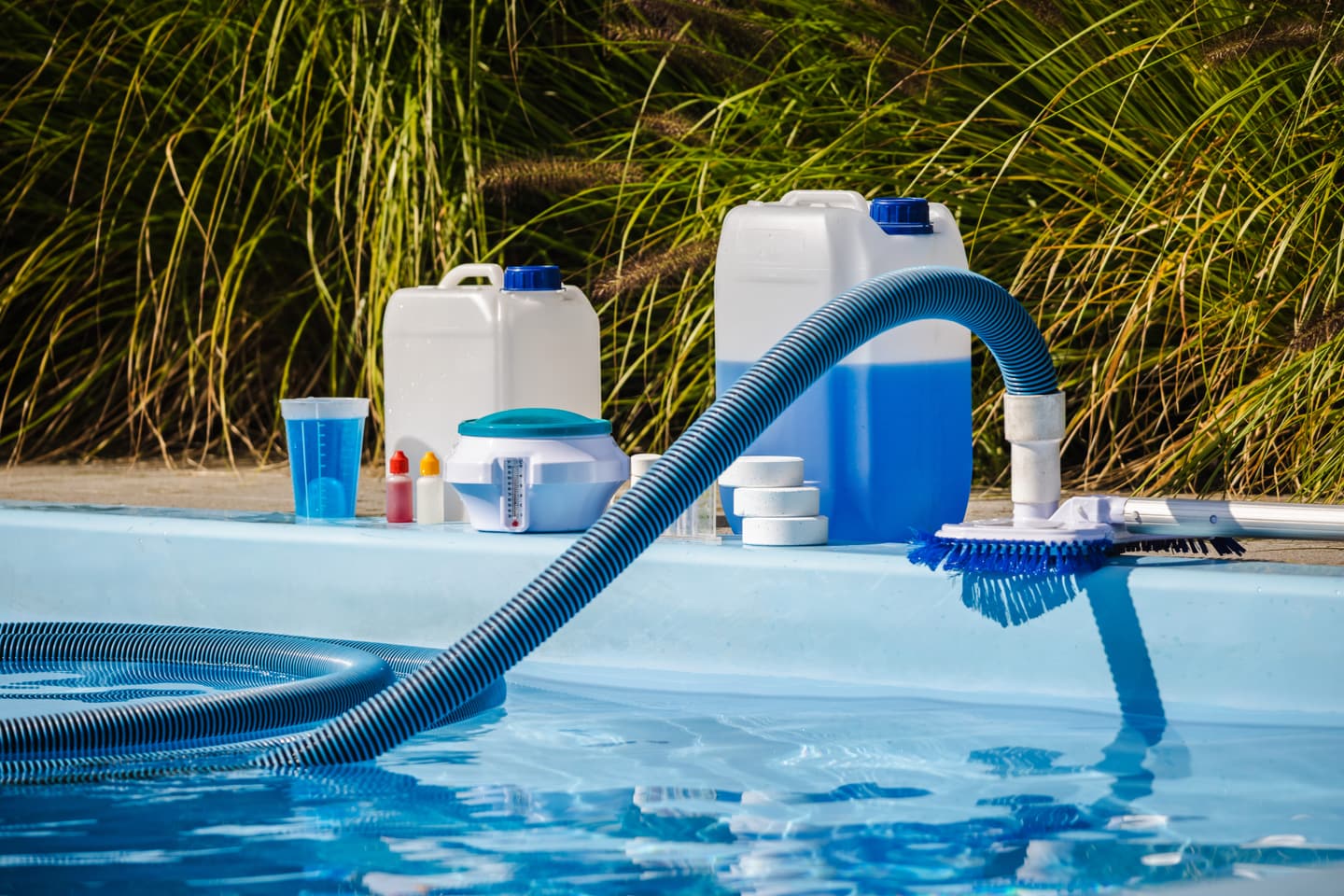 Pool service business technician vacuuming a residential pool mid-visit, with chlorine canisters staged at poolside — a typical pool route stop